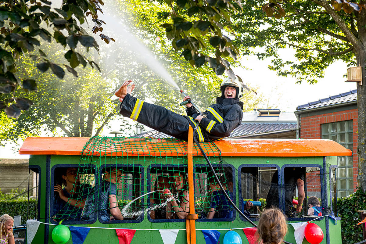 Jordi van der Werf van Werf Events als brandweerblusser op het dak van een voertuig met een werkende brandslang op een kinderfeestje van Kinder Evenementenbureau Drenthe